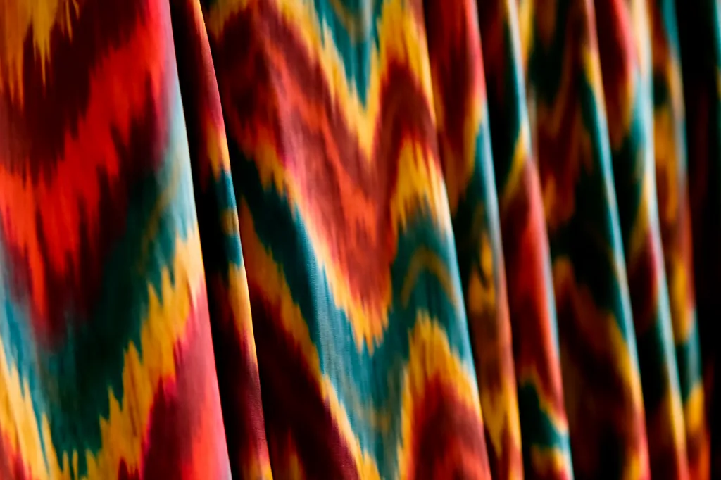 Bolts de soie ikat khan-atlas aux motifs rouges, or et indigo dans un atelier textile ouzbek